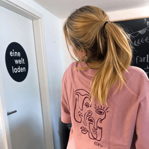 Eine Schülerin zeigt die aktuelle T-Shirt Kollektion 2021 des eineweltladens.