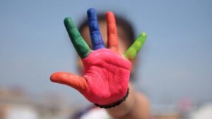 Kind zeigt bunt bemalte Hand; Gesicht unscharf, bunte Farbe fällt auf.