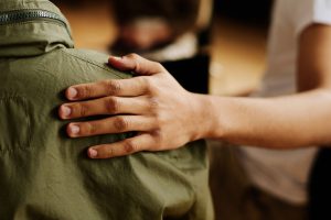 Eine Hand ruht auf einer Schulter und bietet jemandem in einer grünen Jacke Trost.