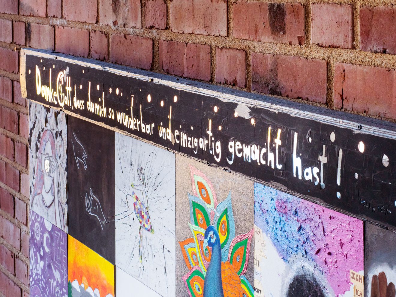 Bunte Kunstfliesen an einer Ziegelwand mit deutschem Dankbarkeitstext darüber in weißen Buchstaben.