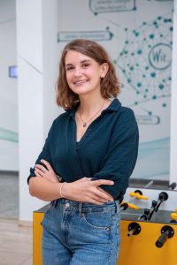 Lächelnde Frau mit kurzen braunen Haaren steht neben Tischfußballtisch und Wissenschaftswandbild. Bild: Fraunhofer IAIS