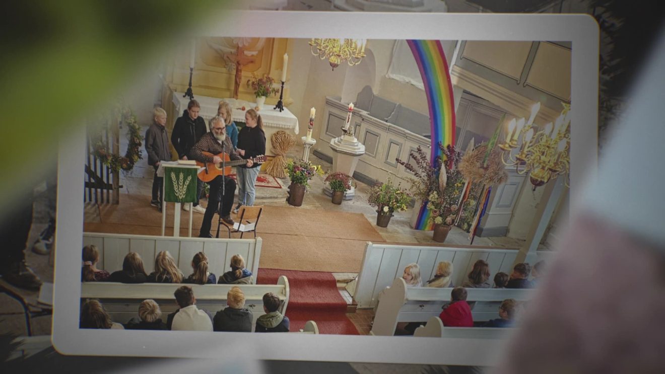 Menschen spielen mit Gitarre vor einem mit einem Regenbogen und Blumen geschmückten Kirchenaltar.