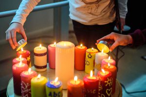 Zwei Personen stellen Teelichter auf einen runden Tisch mit leuchtenden, bunten Stumpenkerzen.