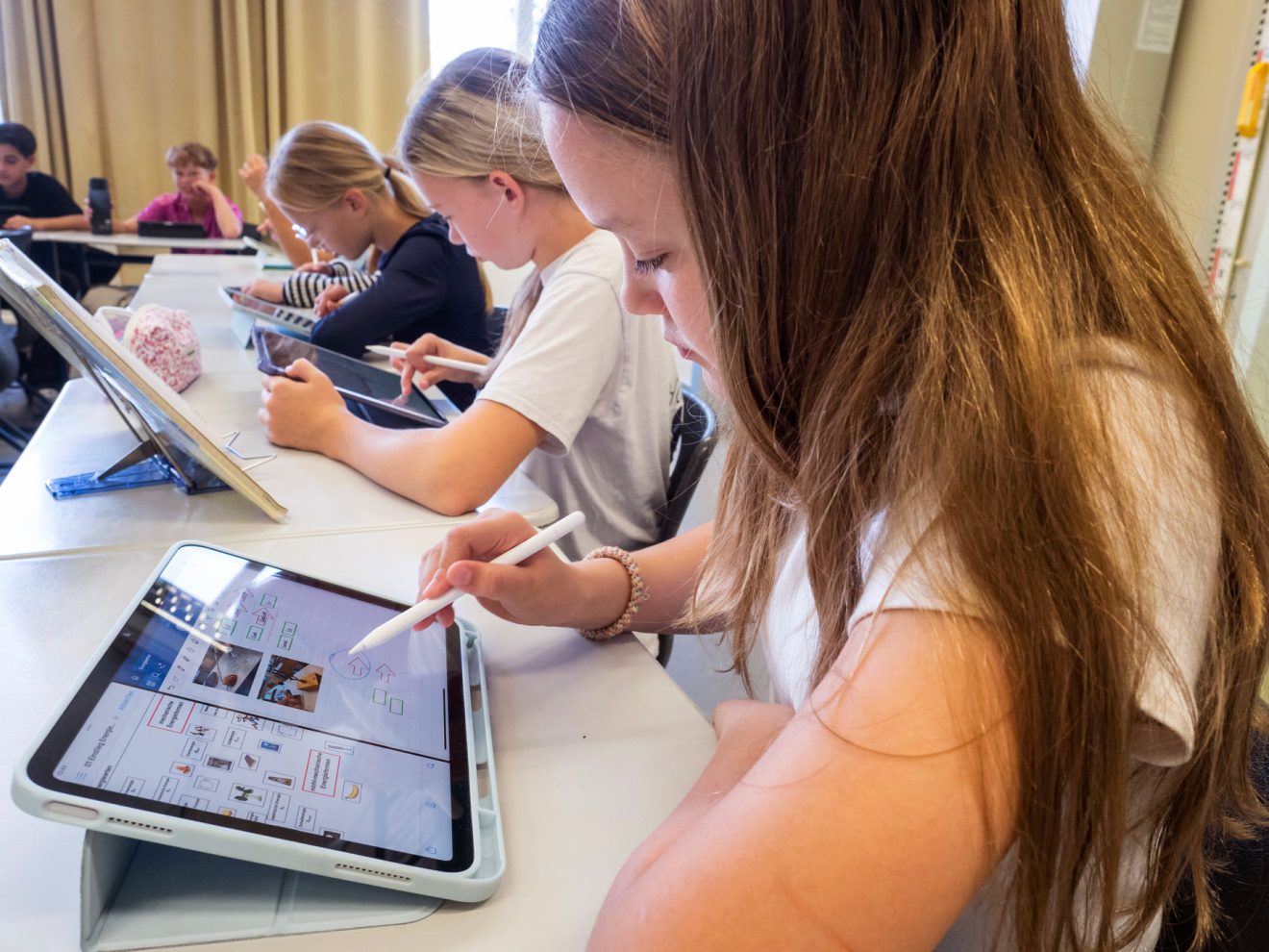 Ein Mädchen zeichnet im Unterricht auf ihrem Tablet, während andere Schüler an ihren eigenen Geräten arbeiten. Foto: Martin Kirchner.