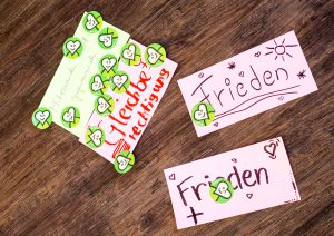 Handgeschriebene Karten mit deutschen Worten und grünen Herzaufklebern auf einer Holzoberfläche.