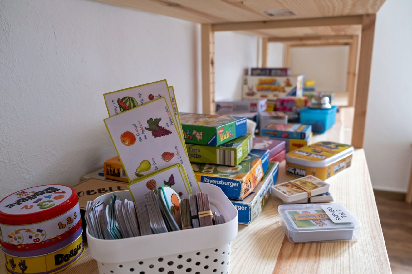 Ein Holzregal mit bunten Brett- und Kartenspielen in einem hellen Raum mit Hartholzboden.