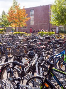 Fahrräder parken vor einer Backsteinschule mit Schülern und Bäumen; auf dem Schild steht "Evangelisches Gymnasium Nordhorn".