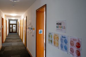 Schulflur mit Klassenzimmertüren und Postern, die deutsche Emotionen mit Cartoon-Gesichtern zeigen.