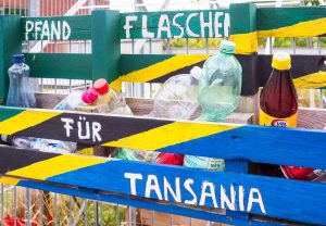Eine gestreifte Sammelbox mit der Aufschrift "Pfandflaschen für Tansania" enthält leere Flaschen.