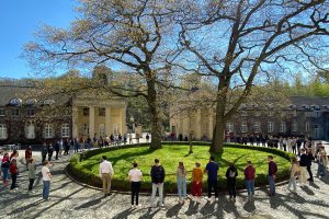 In einem Innenhof mit historischen Gebäuden bilden die Menschen einen weiten Kreis um Gras und Bäume.