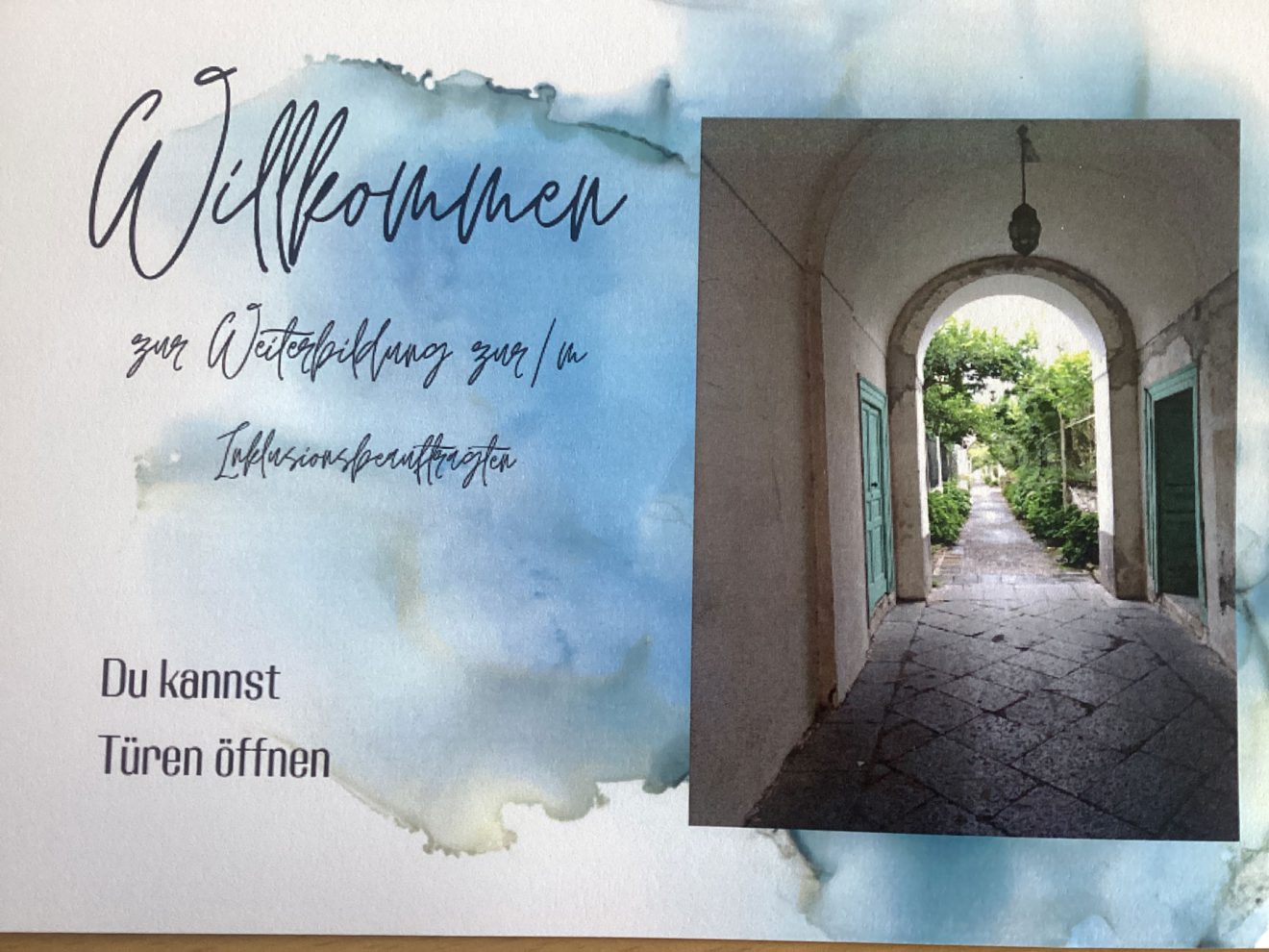 Karte mit blauen Akzenten, deutschem Text und dem Foto eines offenen Torbogens zu einem Garten. Bild: Schulstiftung der Ev.-Luth. Landeskirche Sachsen