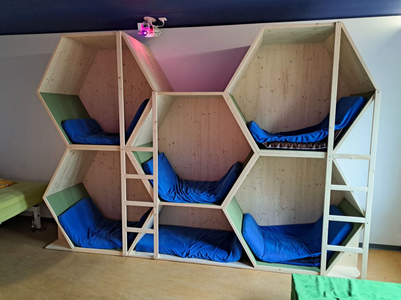 Etagenbett aus Holz mit sechseckigen Schalen, blauen Matratzen und grünen Kissen in einem gemütlichen Zimmer.