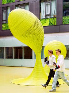 Zwei Jugendliche gehen über einen Innenhof mit einer futuristischen, gelben Skulptur. Foto: Martin Kirchner