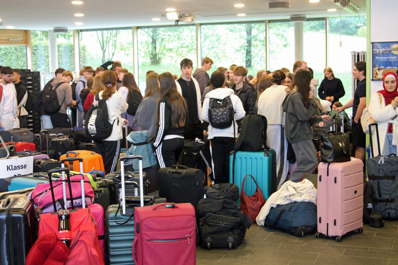 Junge Erwachsene versammeln sich in einem hellen Raum mit bunten Koffern, um sich auf eine Reise vorzubereiten. Bild: Evangelisches Gymnasium Bad Marienberg