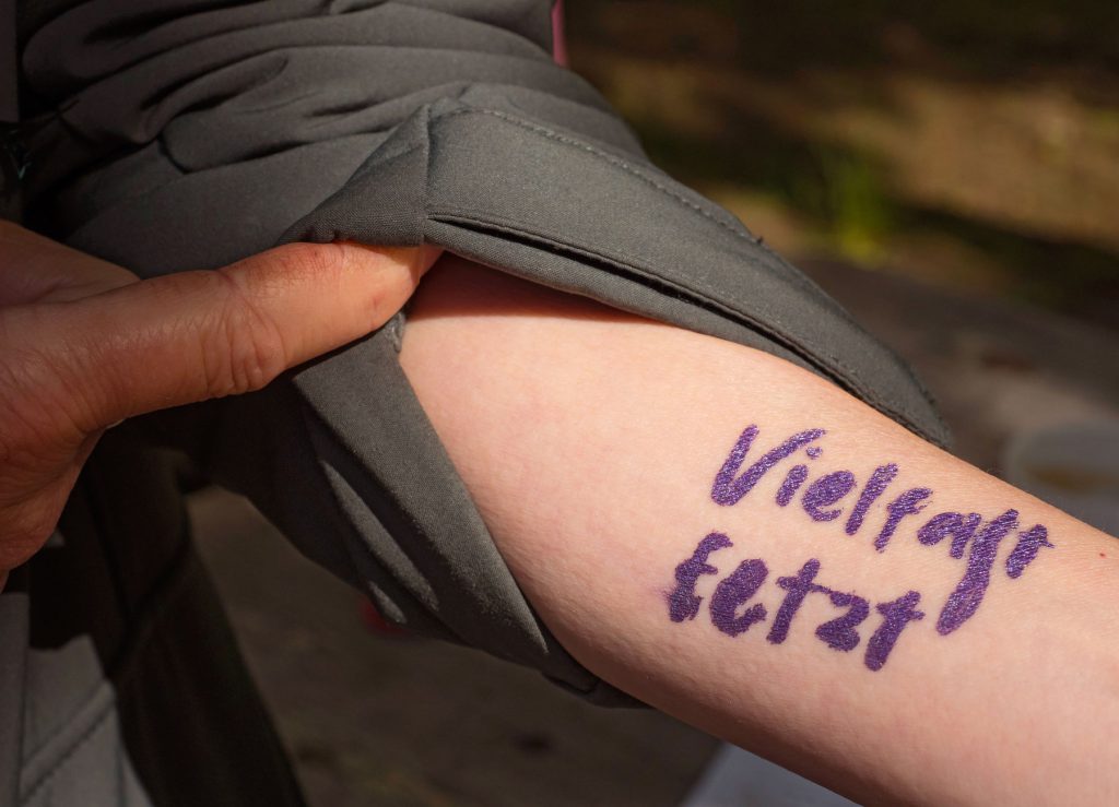 Im Sonnenlicht ist auf dem Unterarm einer Person der mit einem violetten Filzstift geschriebene Schriftzug „Vielfalt jetzt“ zu erkennen. Foto: Martin Kirchner