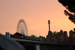 Riesenrad und Hochschaubahn im Sonnenuntergang mit Gebäuden, Felsen und Bäumen im Vordergrund. Bild: Evangelisches Gymnasium Bad Marienberg