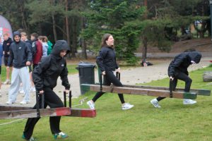 Menschen in Sportkleidung tragen im Freien Holzbalken zusammen, im Hintergrund Bäume. Bild: Evangelisches Gymnasium Bad Marienberg