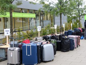 Koffer und Taschen sind unter Klassenschildern vor einem modernen Gebäude mit Bäumen gruppiert. Bild: Evangelisches Gymnasium Bad Marienberg
