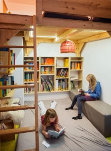 Zwei Kinder lesen in einer gemütlichen Bibliotheksecke mit Holzregalen, bunten Büchern und sanfter Beleuchtung. Foto: Martin Kirchner