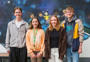 Vier lächelnde Teenager posieren gemeinsam vor einem Wandbild, auf dem sich Comic-Kinder an den Händen halten. Foto: Martin Kirchner
