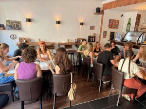 In einem gemütlich beleuchteten Café sitzen die Leute an zwei Tischen und unterhalten sich und schreiben gemeinsam. Foto: Evangelisches Gymnasium Siegen-Weidenau