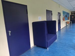 Flur mit blauen Türen, einem Sofa, einem Boden, beigen Wänden und einem farbenfrohen Wandbild.