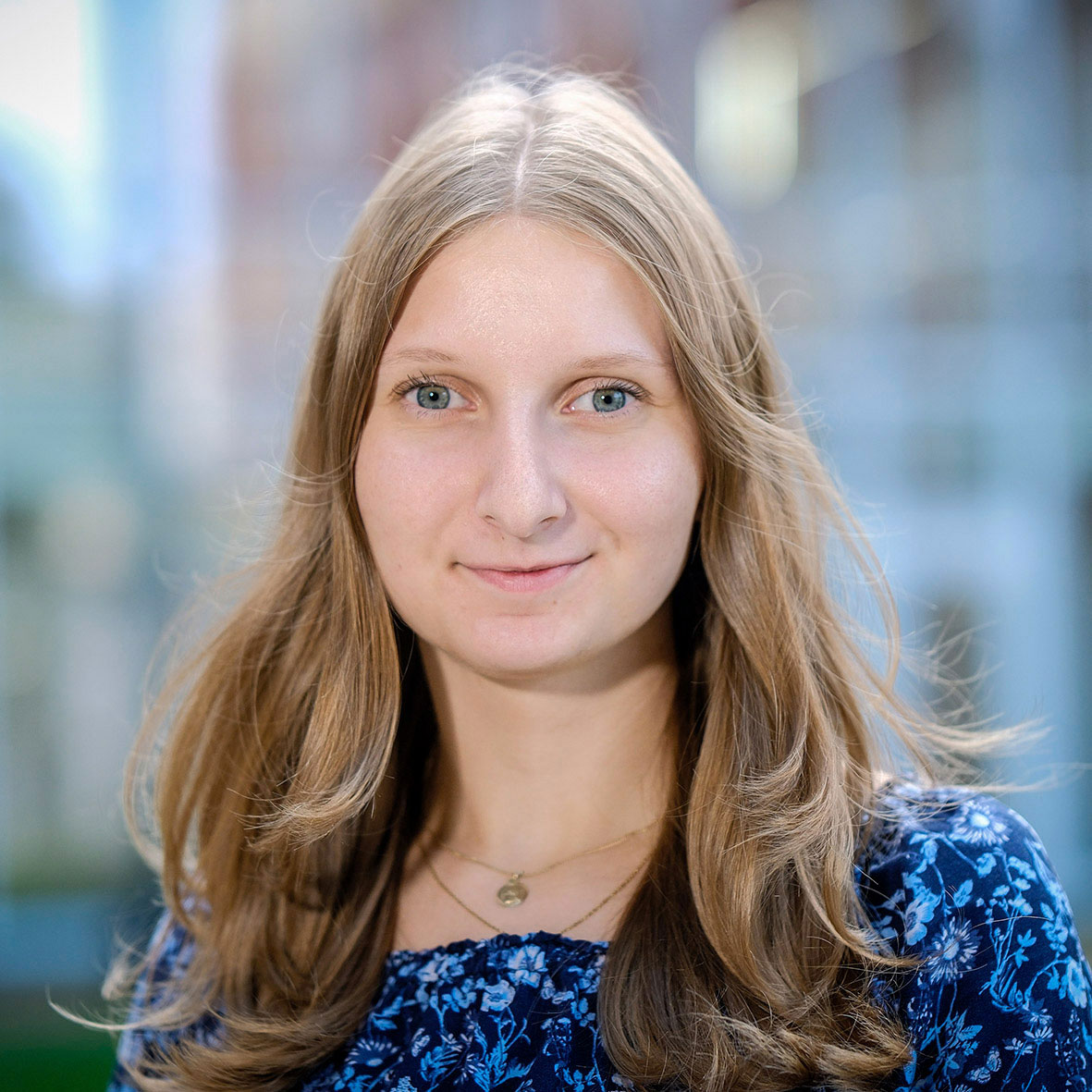 Junge Frau mit hellbraunen Haaren und blauen Augen in einer blauen Bluse im Freien.
