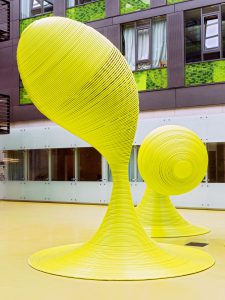 Zwei abstrakte gelbe Ringskulpturen in einem modernen Raum mit Glaswänden und grünen Akzenten. Bild: Martin Kirchner