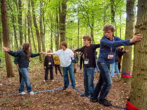 Vier Menschen balancieren auf blauen Seilen, die zwischen Bäumen in einem Wald gespannt sind. Bild: Martin Kirchner