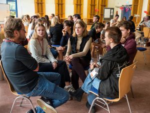 Eine kleine Gruppe junger Leute sitzt in einem großen Raum im Kreis und unterhält sich. Bild: Martin Kirchner